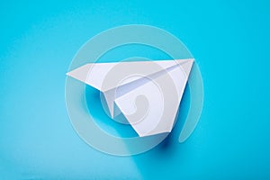 White paper origami airplane lies on pastel blue background