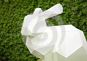 White paper rabbit on a background of green moss. Easter bunnies origami .