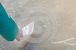 White paper ship is sent on journey into first spring puddle. Child`s hand with origami in sunlight. Early spring mood concept,