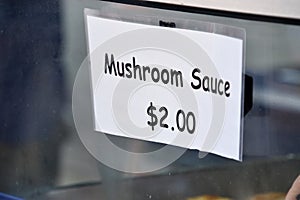 A white paper sign on a glass case the says Mushroom Sauce $2.00