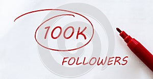 White paper with text 100K Followers on the white with red marker