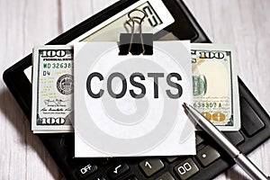 White paper with text COSTS with dollars on calculator