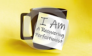 White paper with text I Am A Recovering Perfectionist on the black cup photo