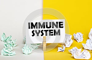 White paper with text Immune System on a clothespin on yellow and white backgrounds with paper wads of different colors