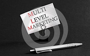 White paper with text MLM Multi-Level-Marketing on a black background with stationery