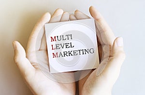 White paper with text MLM Multi Level Marketing in male hands on a white background