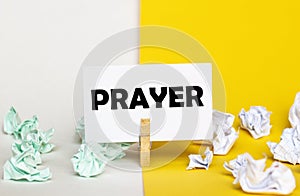 White paper with text Prayer on a clothespin on yellow and white backgrounds with paper wads of different colors
