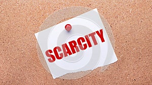 White paper with the text SCARCITY is attached to the wooden background with a red button