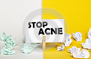 White paper with text Stop Acne on a clothespin on yellow and white backgrounds with paper wads of different colors