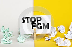 White paper with text Stop Fgm on a clothespin on yellow and white backgrounds with paper wads of different colors