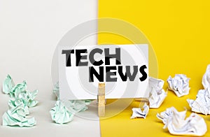 White paper with text Tech News on a clothespin on yellow and white backgrounds with paper wads of different colors