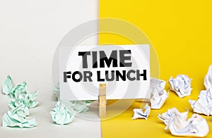 White paper with text Time For Lunch on a clothespin on yellow and white backgrounds with paper wads of different colors