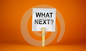 White paper with text `Whats next`, clip on wood clothespin. Beautiful orange background. Business concept. Copy space