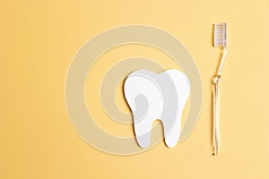 White paper tooth with toothbrush on yellow background. Dental health concept. Dentist day concept