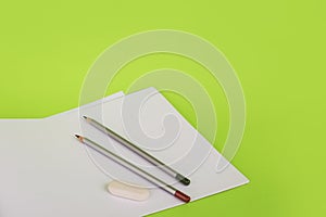 White paper and two pencils on a green background. Album for drawing and pencils. The artist draws. stationery on a green