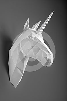 White paper unicorn`s head hanging on dark graphitic shadowed wall.