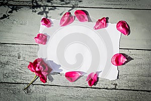 White paper on wooden background and red rose petals