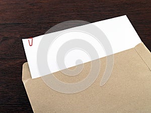 white paperwork with red clip in brown envelope on dark brown wooden desk floor