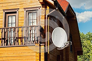White parabolic satellite antena dish hanged on wall of modern wooden country house villa. Wireless television
