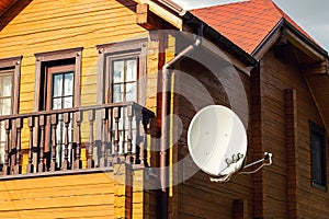 White parabolic satellite antena dish hanged on wall of modern wooden country house villa. Wireless television broadcasting