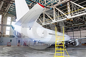 White passenger aircraft in the hangar. Airplane under maintenance. Checking mechanical systems for flight operations