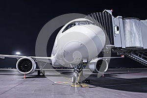 A white passenger airplane stands at the jetway connected to an external power supply on an airport night apron