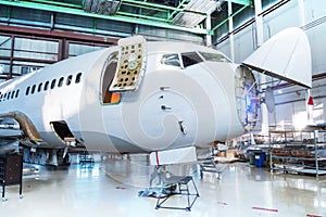 White passenger airplane under maintenance in the hangar. Checking mechanical systems for flight operations. The aircraft has