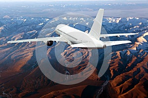 White passenger plane flies above the  mountain landscape. Back view.