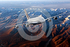 White passenger plane flies above the mountain landscape. Front view.