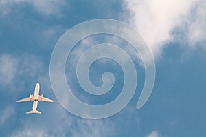 White passenger plane flies against the background of a bright blue sky with clouds