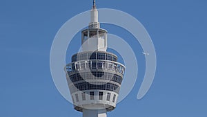 White passenger plane in flight in the distance in the background blue sky. Aircraft flies over the Air Traffic Control tower.