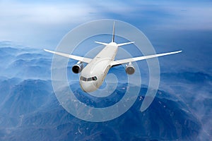 White passenger plane fly above the mountain landscape. Front view of aircraft