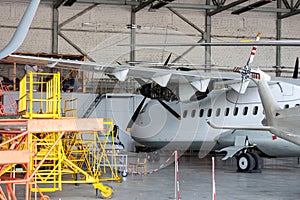 White passenger turboprop airplane under maintenance in the hangar. Repair of aircraft engine on the wing and checking mechanical