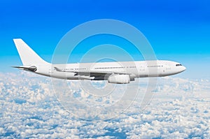 White passenger wide-body aircraft flies travel, trip at the flight level cumulus clouds, above against the blue sky.