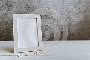 White pastel frame with LOVE letter on the white wooden table with black background. Minimal and simple composition for wallpaper.