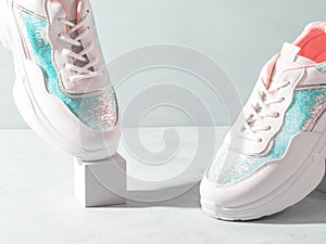 White pastel sneakers with sequins on geometric podiums on turquoise