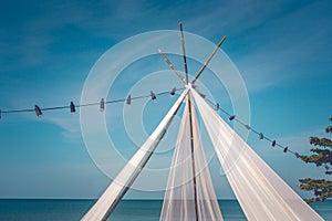 White pavilion on sand beach and row of light bulb hanging on electric wire with beautiful seascape view and blue sky