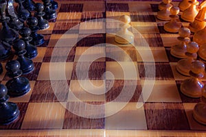White pawn staying against full set of black chess pieces. Closeup of chessboard with wooden pieces on table in sunlight, game of