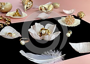 White pearl jewelry gold rings on a black background with pink opal in seashell , precious stones, rose petals and feathers concep