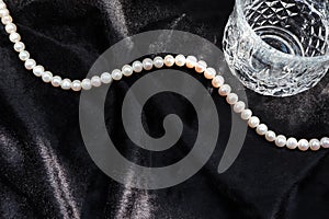 White pearls necklace and glass on black flannel.