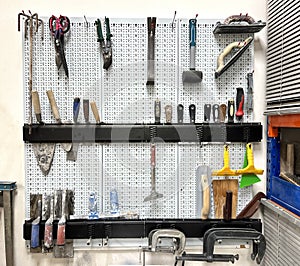 White pegboard wall with a set of different tools in a workshop photo