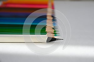 A white pencil with a black tip lies next to colored pencils folded in a row.