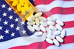 White pharmaceutical pills spilling from prescription bottle over American flag