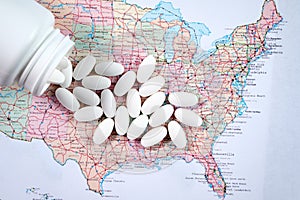 White pharmaceutical pills spilling from prescription bottle over map of America background