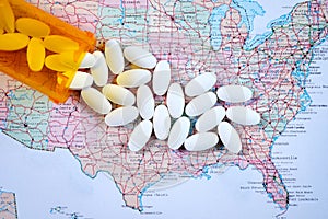 White pharmaceutical pills spilling from prescription bottle over map of America background