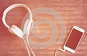 White phone and headphones flat lay on wooden table. Warm orange light toned photo.