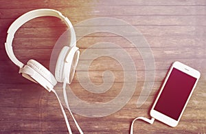 White phone and headphones on wooden table. Warm yellow toned photo.