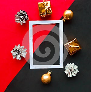 White photo frame and golden Christmas decorations on geometric red and black abckground. Flat lay, top view, copy space.