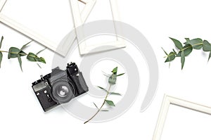 White photo frame, old retro photo camera and green eucalyptus leaves on white background. Flat lay top view copy space. Stylish
