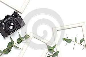 White photo frame, old retro photo camera and green eucalyptus leaves on white background. Flat lay top view copy space. Stylish